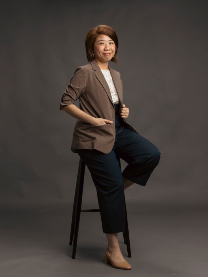 Lay Hiang in a brown blazer, sitting on a tall stool